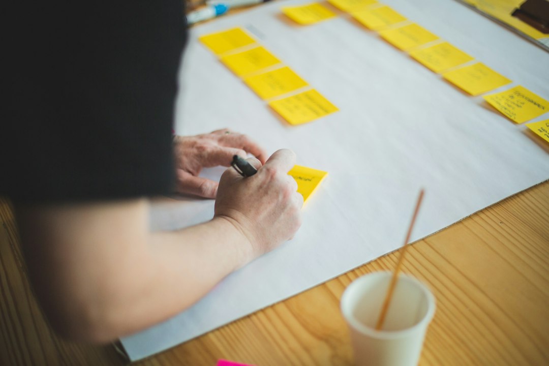 A person writing on a sticky note during a business planning session, illustrating AI moderation cost analysis